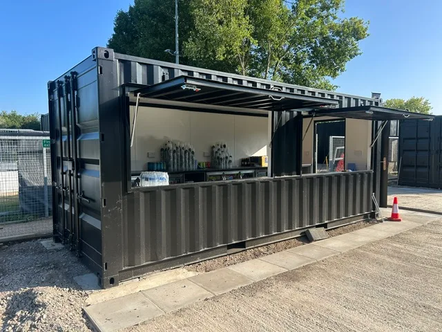 Anthracite 20ft shipping container bar with the fold-up canopy side raised over a serving counter, set up outdoors