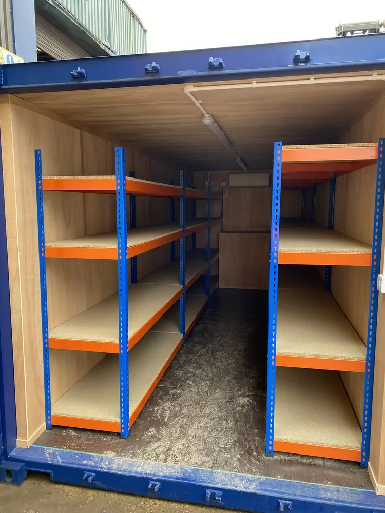 Open doors of a converted battery storage container showing two rows of heavy-duty racking and a lined interior