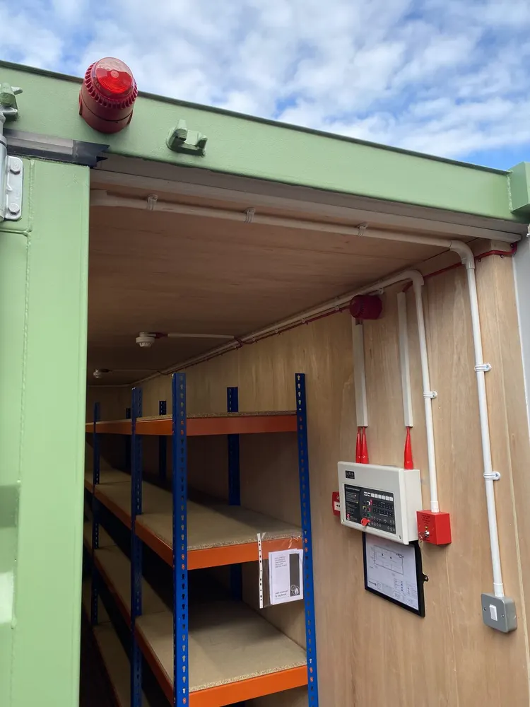 Doorway of a converted battery storage container with an external alarm beacon above and racking visible inside