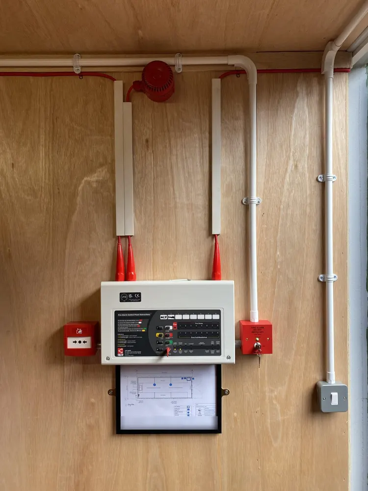 Fire-alarm control panel, manual call point, sounder and key switch mounted on the lined wall of a battery storage container