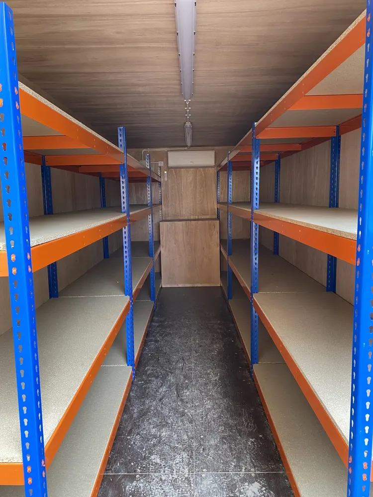 Inside a battery storage container conversion — heavy-duty racking along both walls with air conditioning at the far end